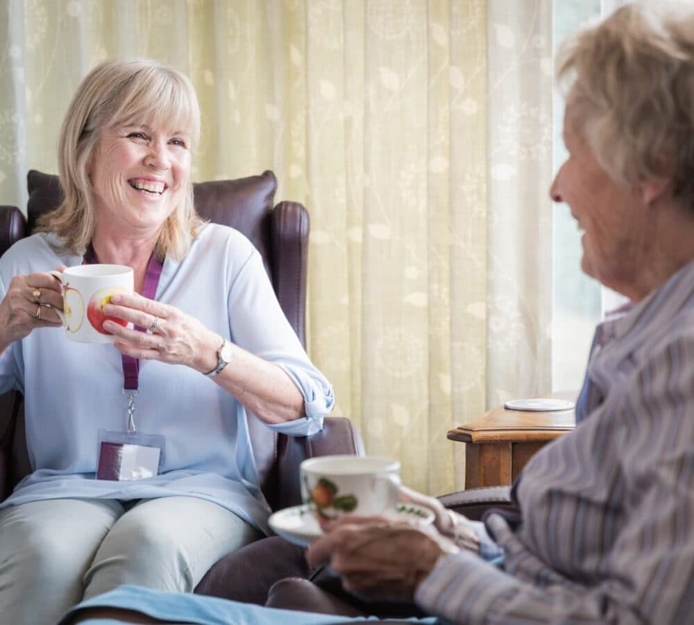 Older adult happy while enjoying a cup of tea with her carer