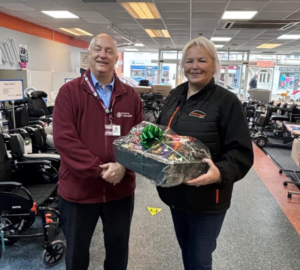 A woman holding a hamper inside a mobility shop with a man from Home Instead wearing Home Instead jacket