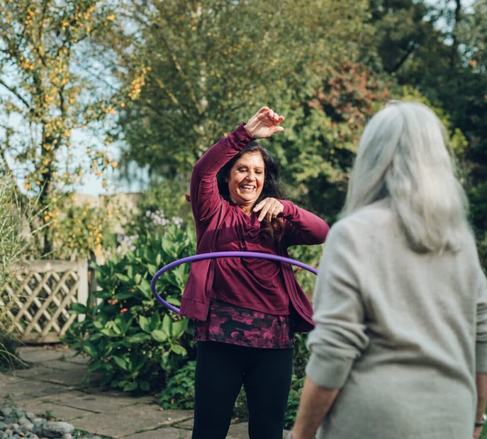Older woman watching her carer playing hula hoop outdoors