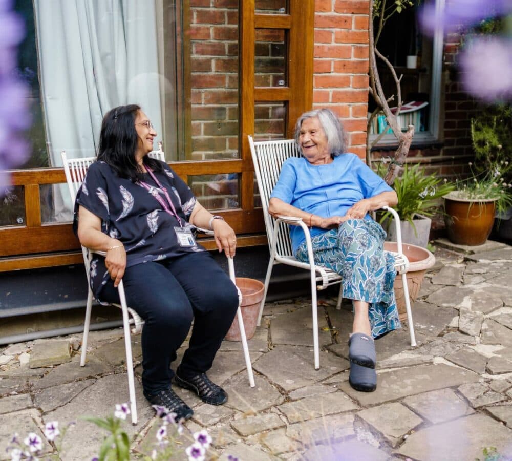 Two women sitting down and relaxing while chatting outside the house