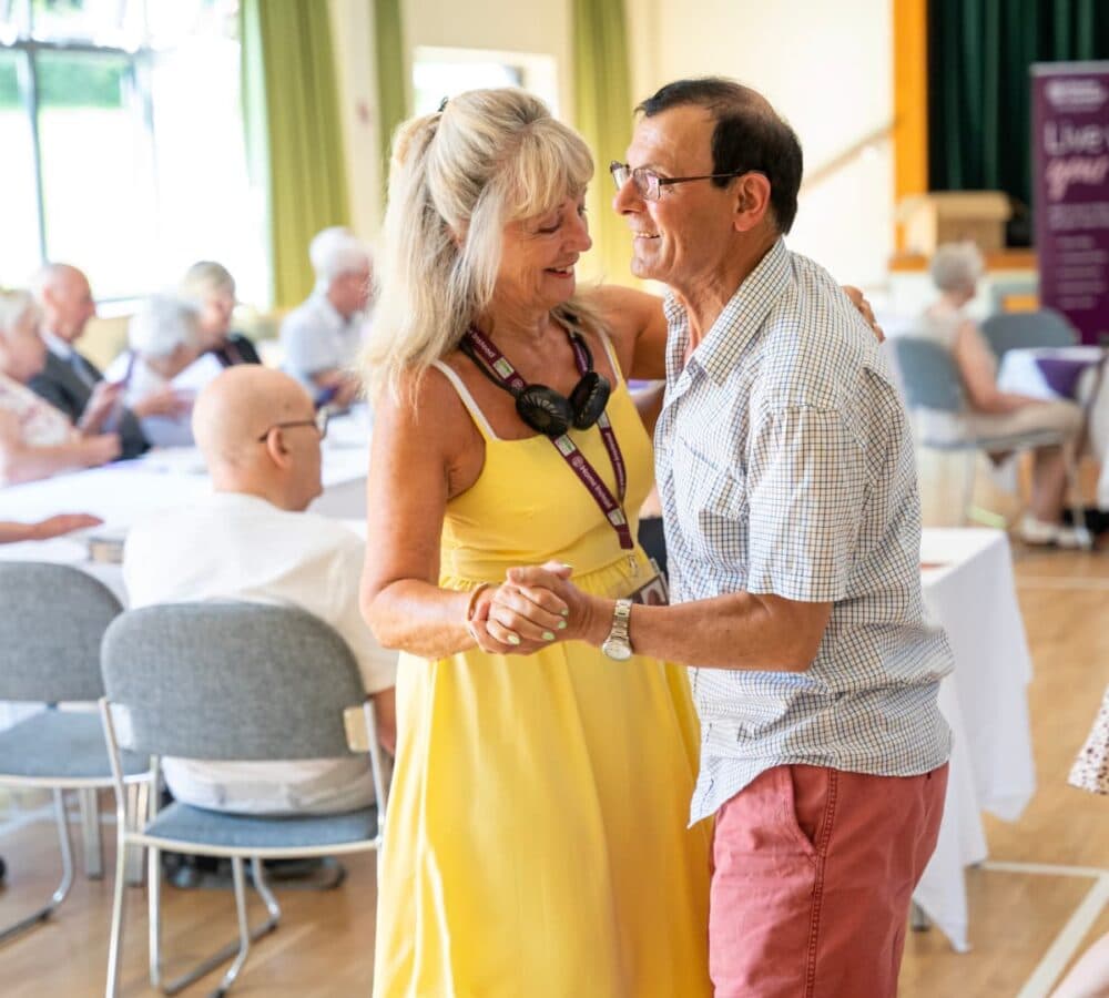 An older woman wearing yellow dress dancing with an older man inside the hall