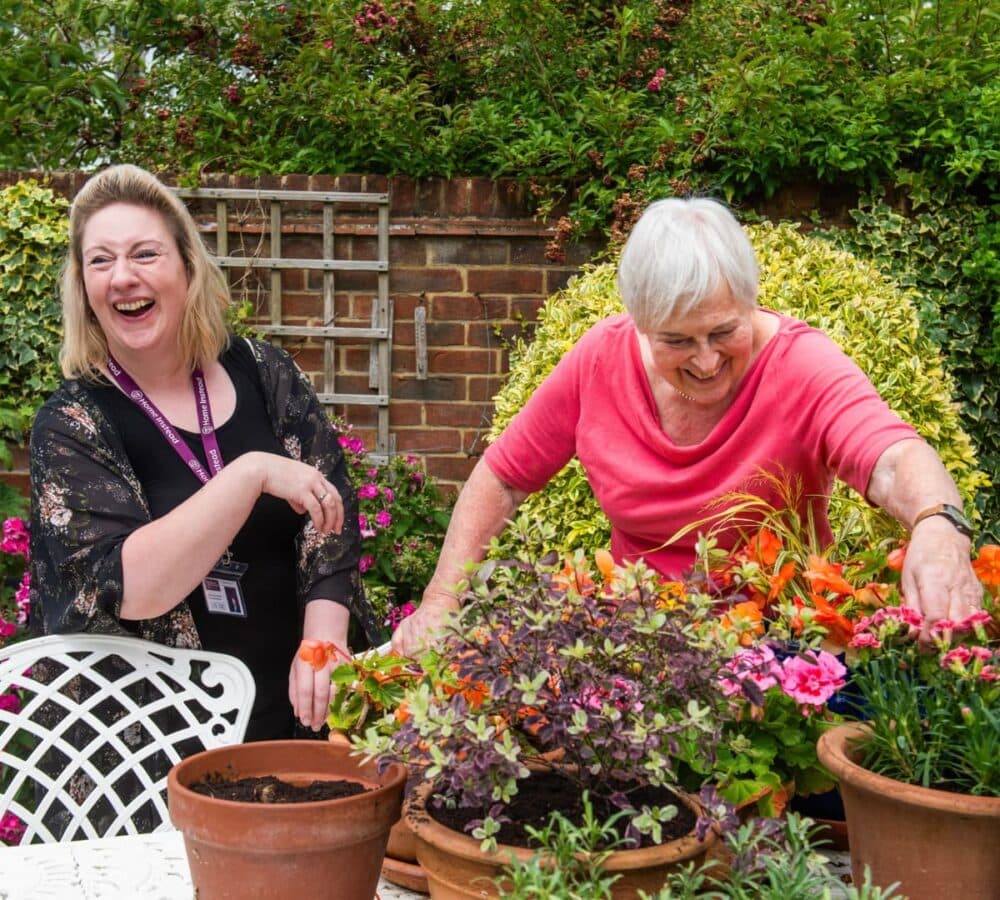older woman with short white hair gardening her beautiful flowers with her carer