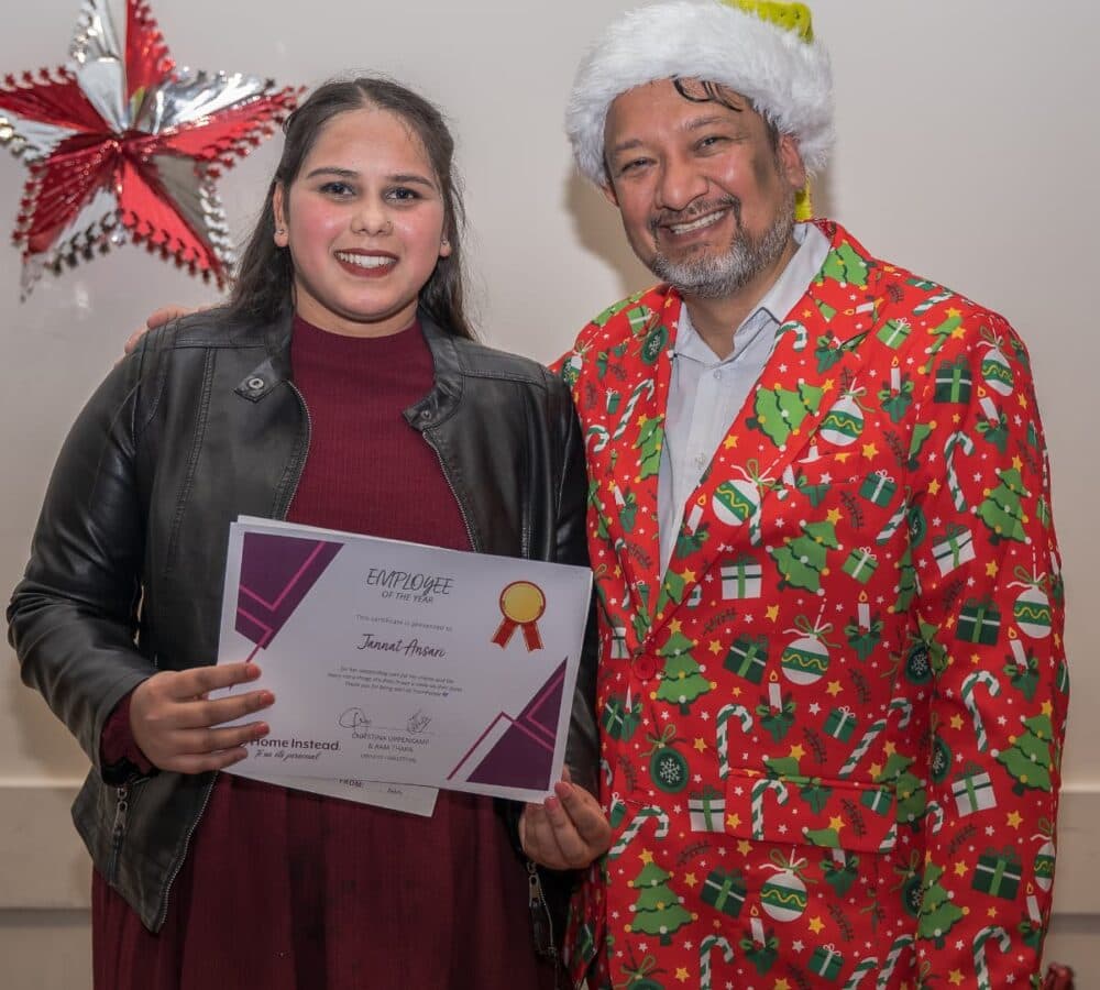 A woman holding a certificate with an older man wearing Santa hat and colorful clothes