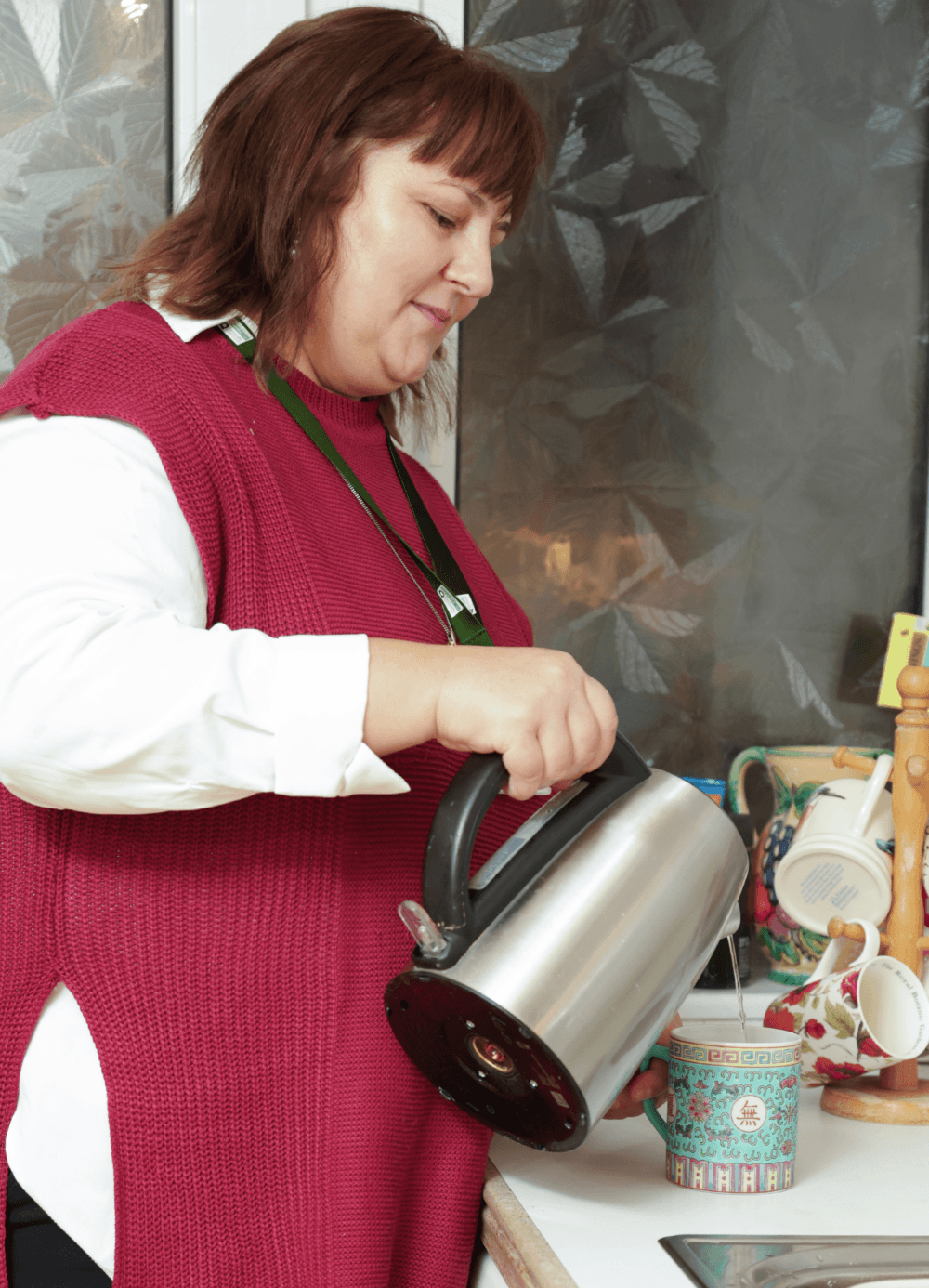 Woman in a red sweater pouring hot water from a kettle into a mug in a kitchen. - Home Instead