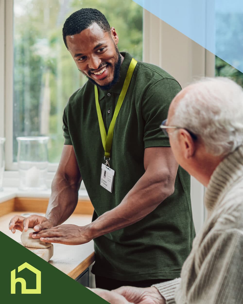 A caregiver smiles while helping an elderly man in a kitchen, both engaged in conversation. - Home Instead