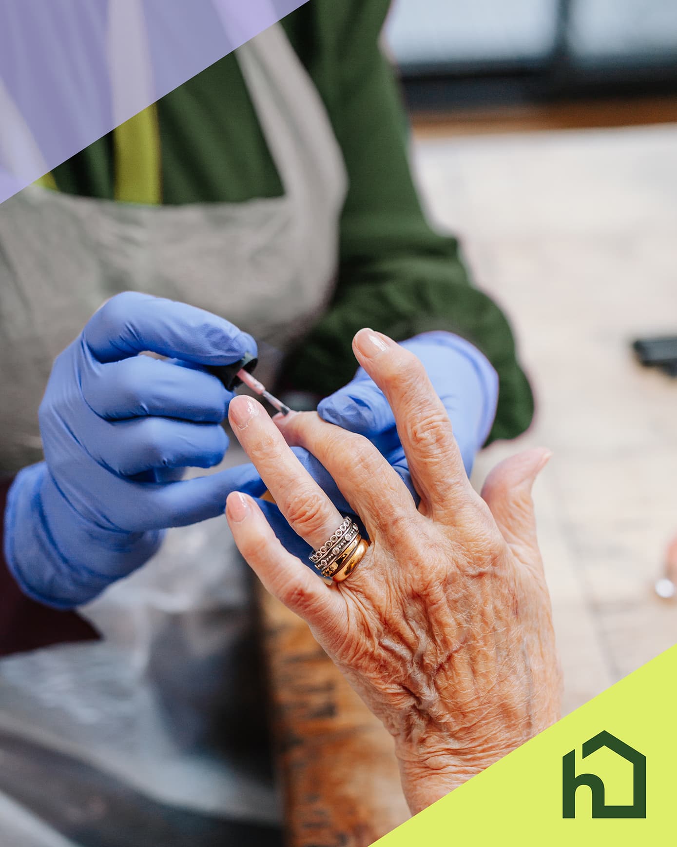 A person wearing gloves applies nail polish to an elderly person’s hand at a table, with a green house logo in corner. - Home Instead