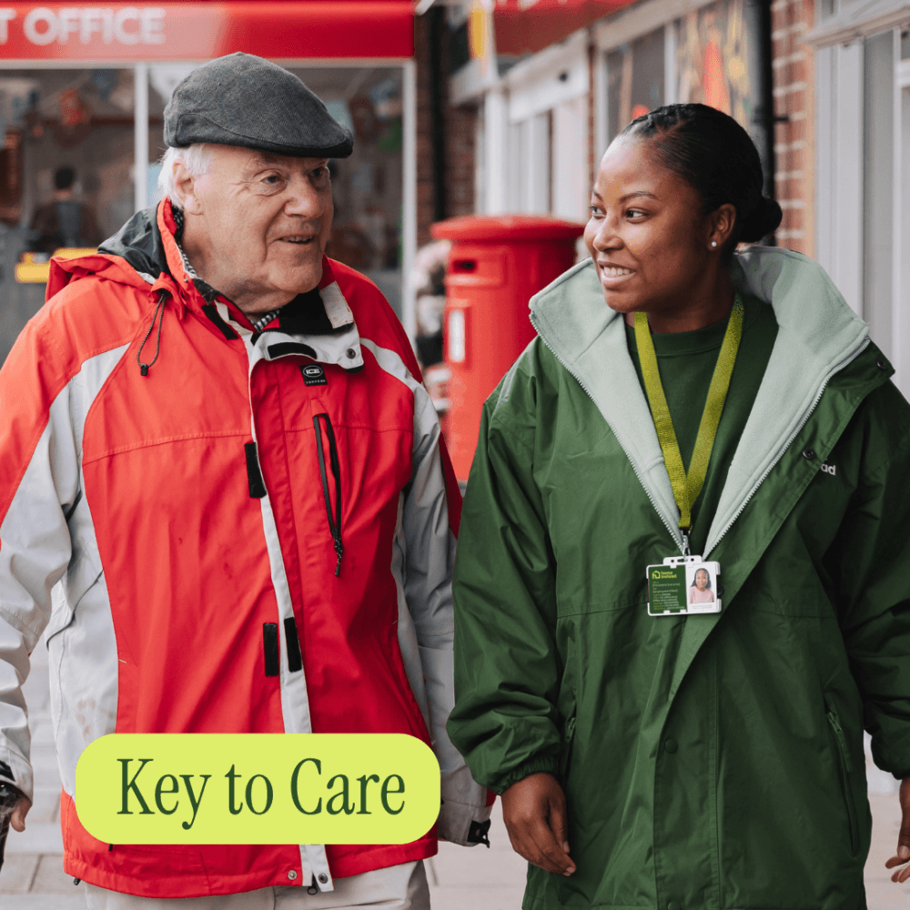 An elderly man and a caregiver walk together outside, both smiling. Text reads "Key to Care. - Home Instead
