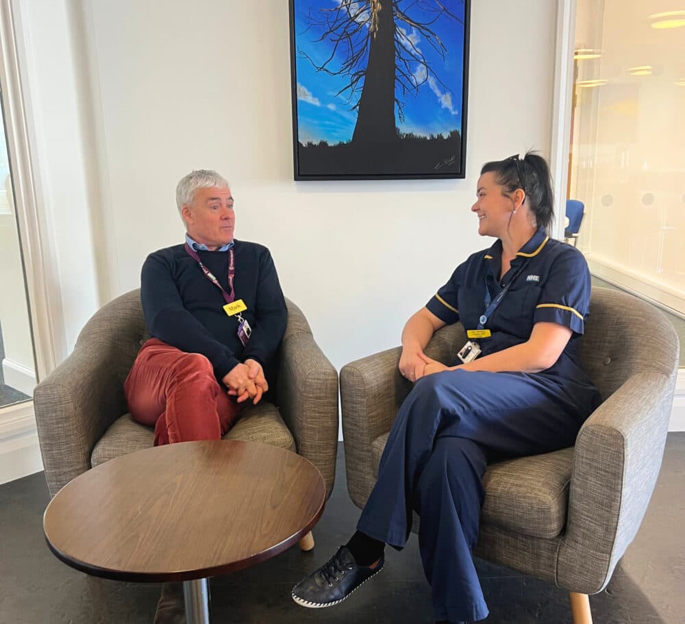 Mark and Lilly talking, in an office setting