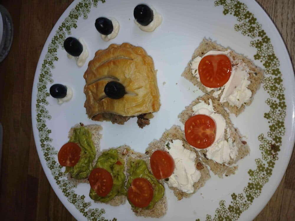 A decorated plate with puff pastry, bread slices topped with spread and cherry tomatoes, and olives on cream. - Home Instead