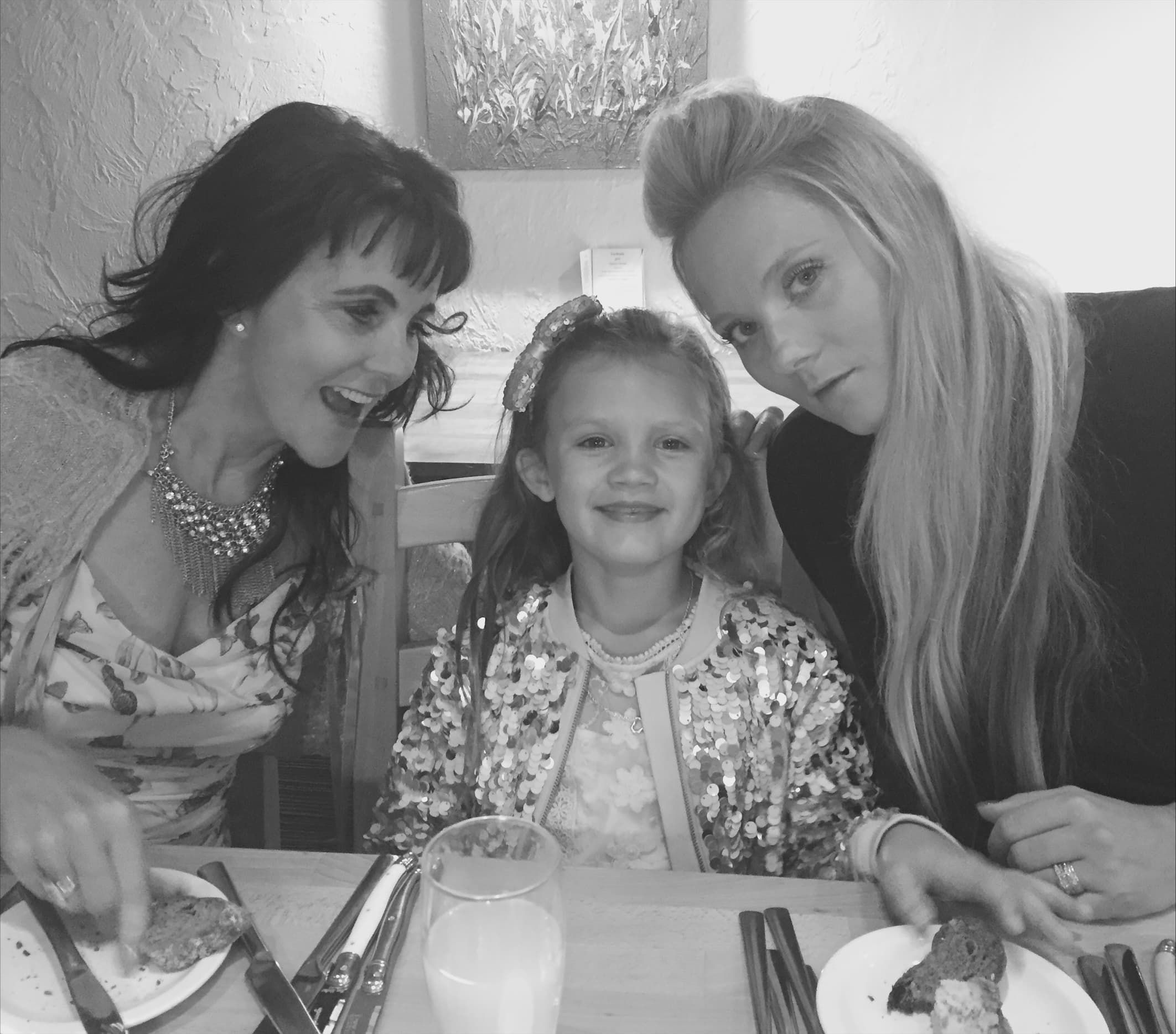 Three people, two women and a girl, sit together smiling at a table with food and drinks. - Home Instead