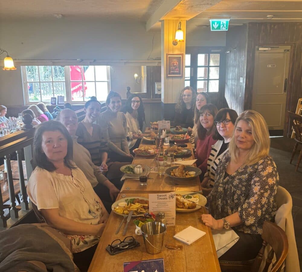A group of women sitting with long table and with lots of food all happy and smiling inside the restaurant