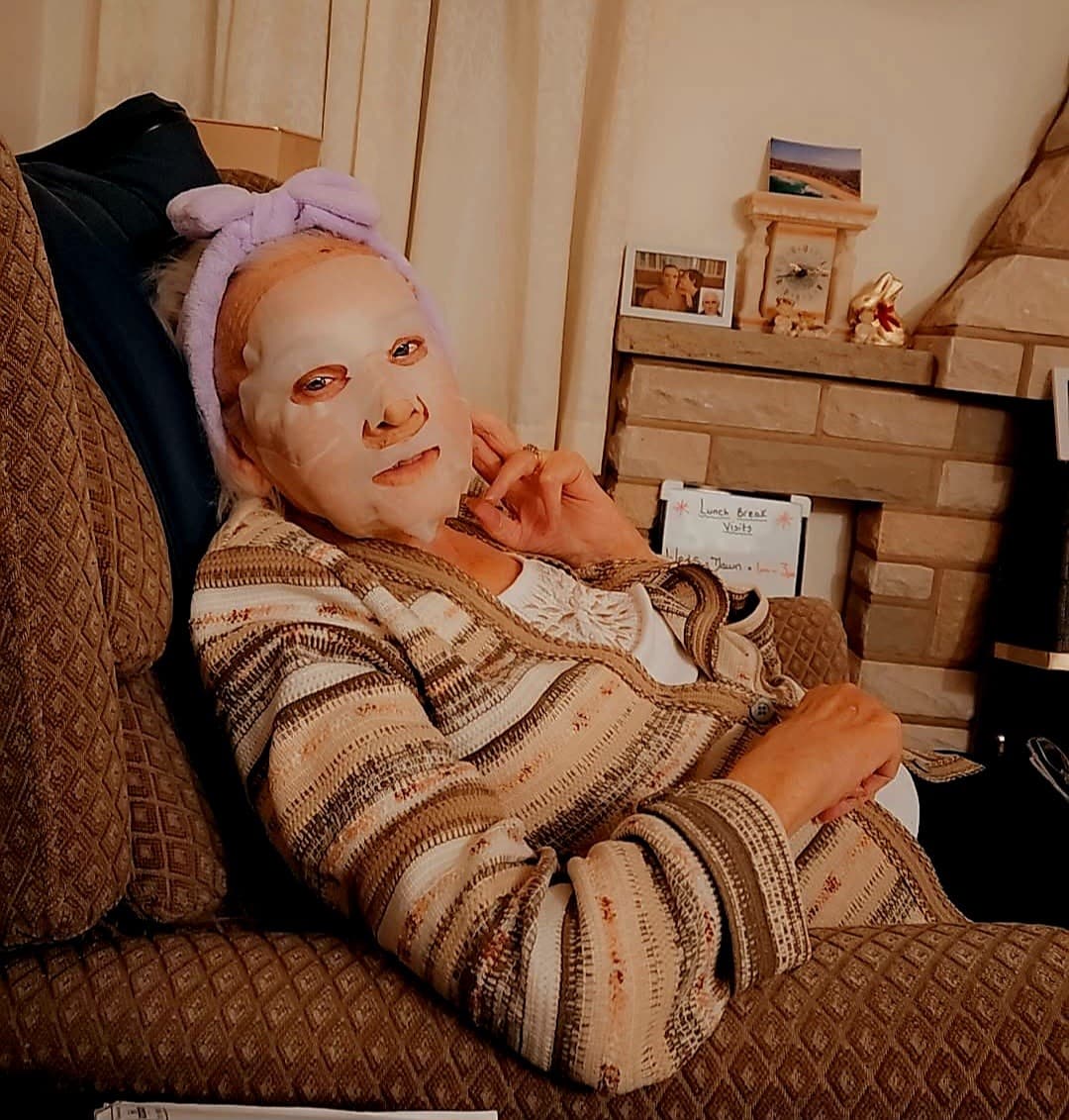 Woman relaxing on a couch with a face mask and headband, wearing a striped sweater in a cozy living room. - Home Instead