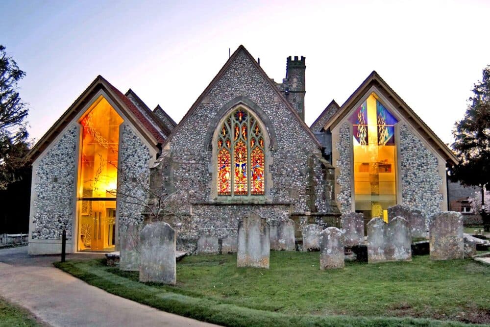Stone church with colorful stained glass windows, glowing lights inside, and gravestones in the foreground. - Home Instead