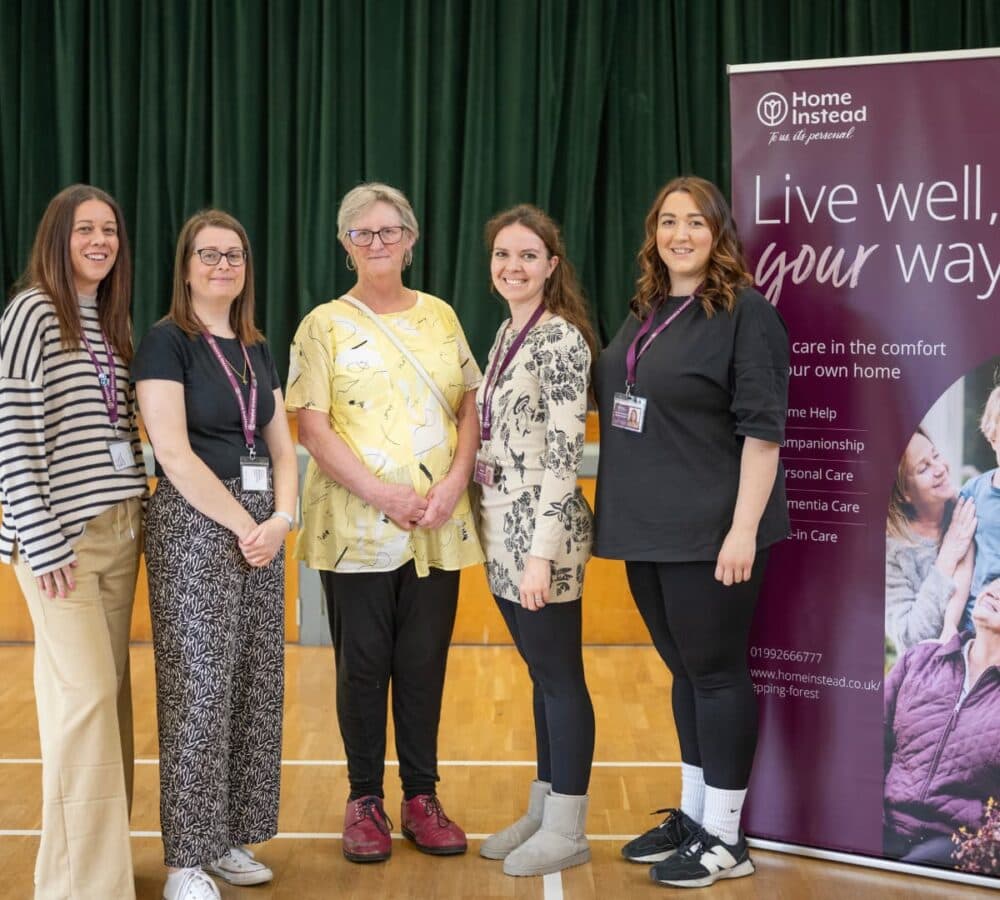 Women standing and smiling with a Home Instead standee at the side