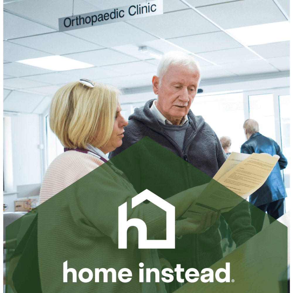 A woman helps an older man with papers in an orthopaedic clinic. "Home Instead" logo is overlaid. - Home Instead