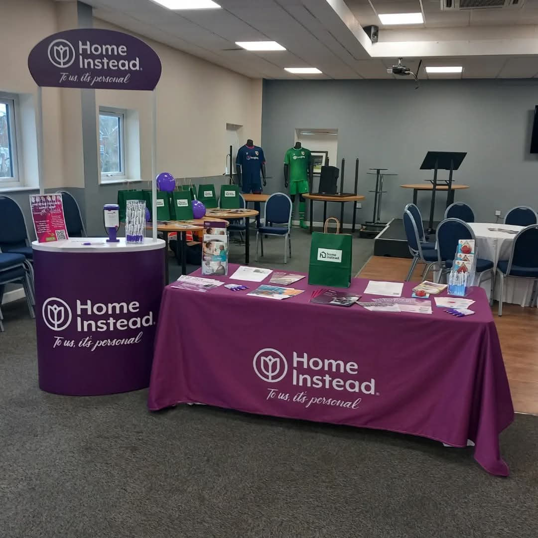 Home Instead display booth with brochures and promotional items in a conference room setting. - Home Instead