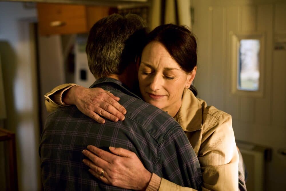 A woman with closed eyes hugs a man indoors, expressing comfort and warmth. - Home Instead