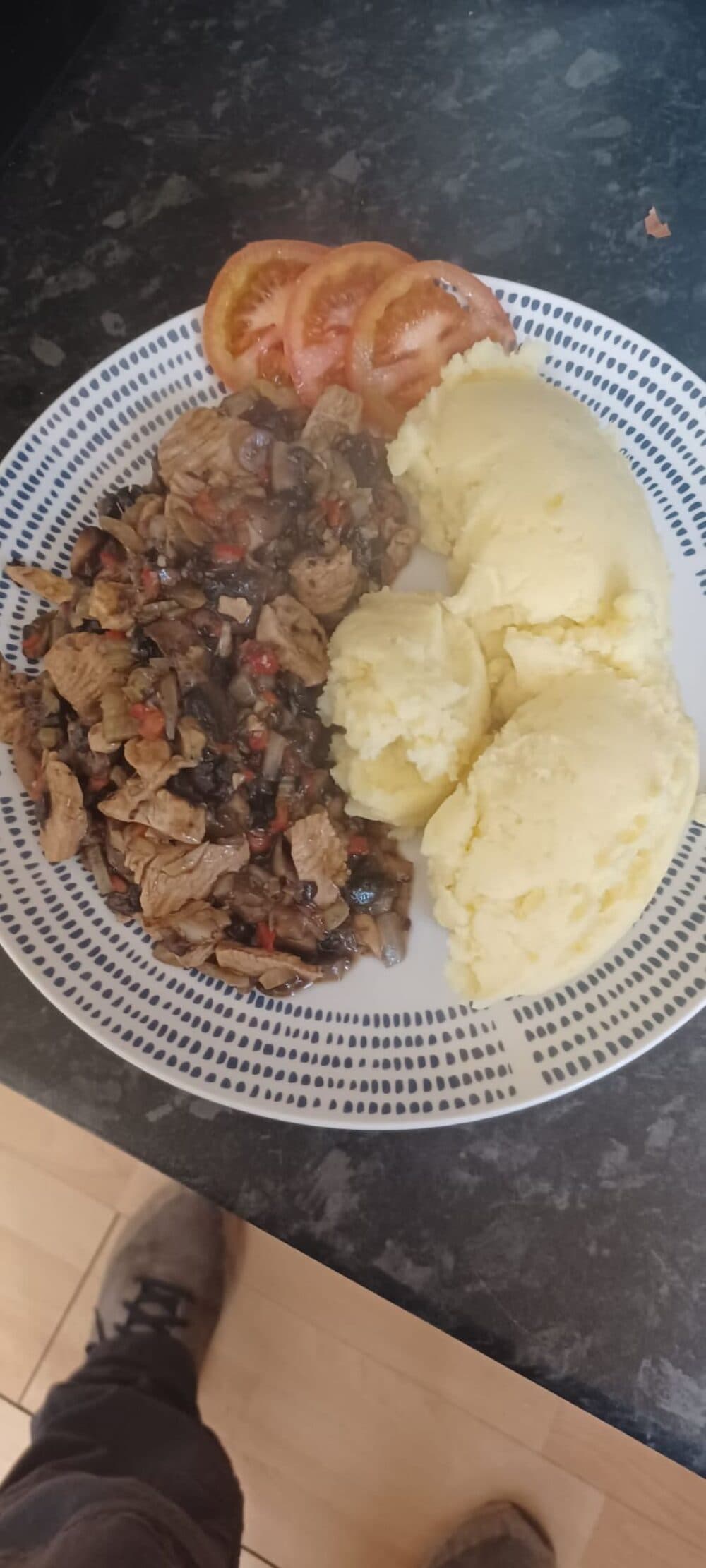 A plate with mashed potatoes, cooked meat with vegetables, and sliced tomatoes on the side. - Home Instead