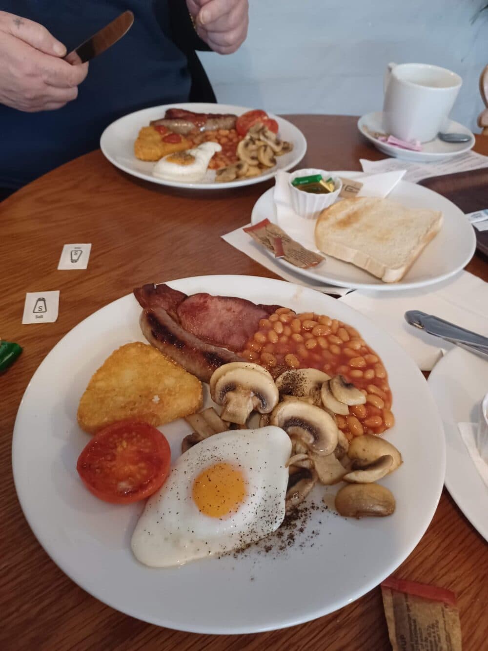 A full English breakfast with egg, bacon, beans, mushrooms, hash brown, tomato, and toast on a table. - Home Instead