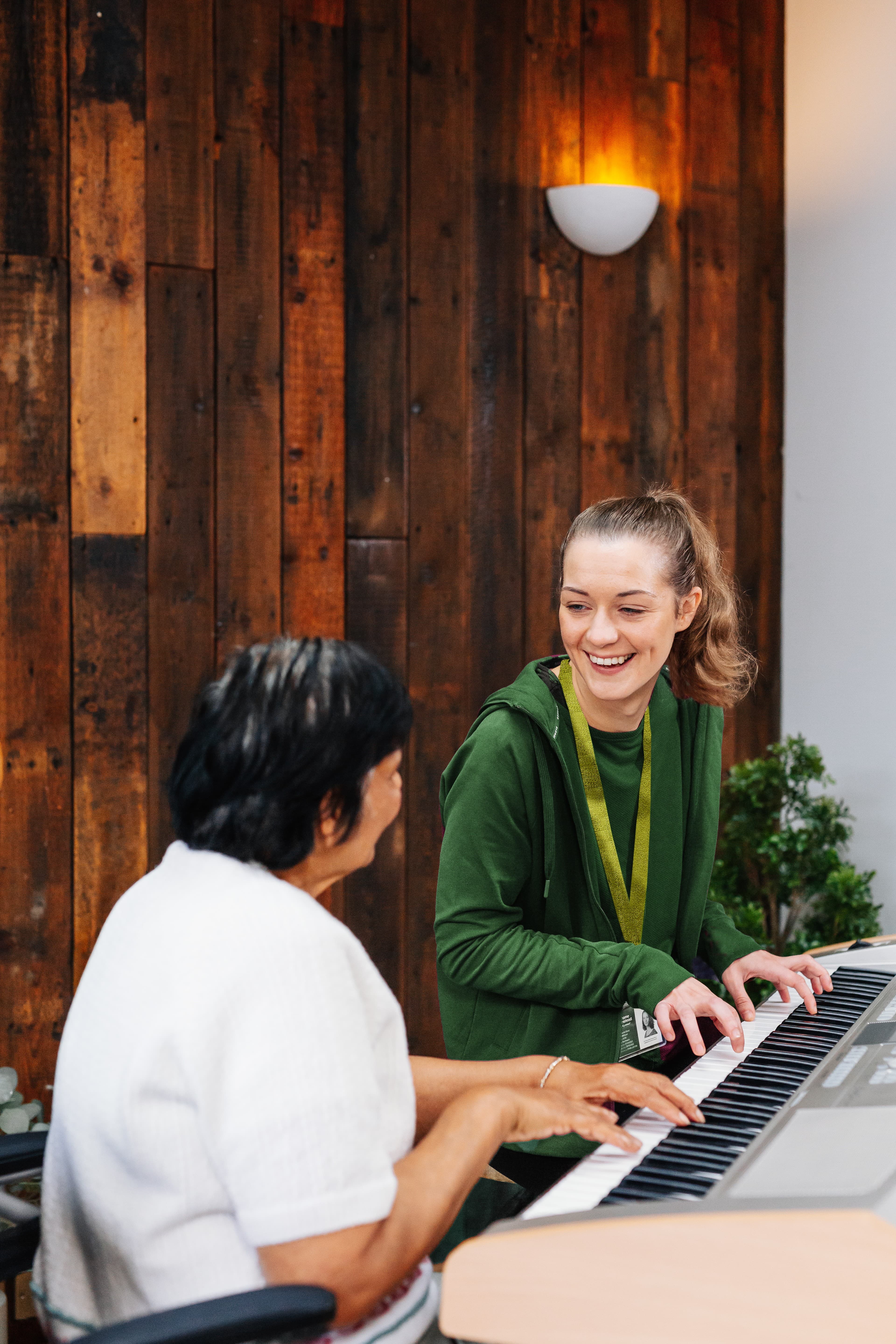 Three people smiling, one holding a certificate and another holding flowers. A sign on the wall reads "Reliable. - Home Instead