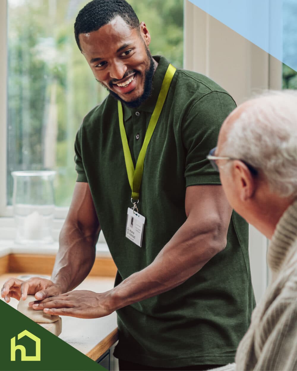Smiling caregiver chats with an elderly man in a bright kitchen, wearing an ID badge and green shirt. - Home Instead