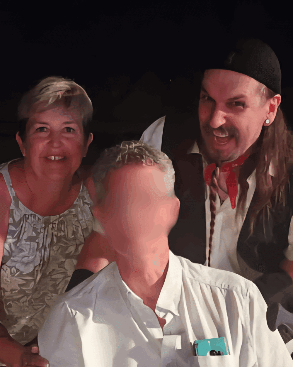 Two people smiling next to a person in a pirate costume; the center person's face is blurred. - Home Instead