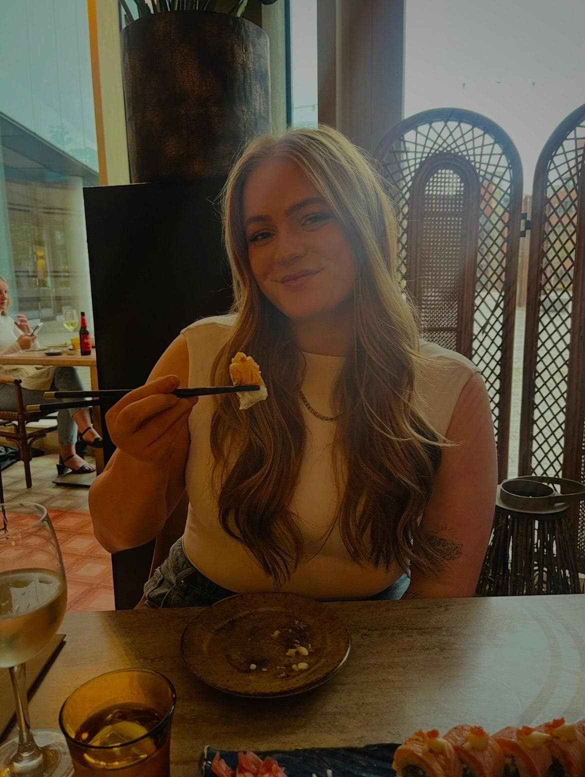 A woman with long hair smiles and holds sushi with chopsticks at a restaurant table. - Home Instead