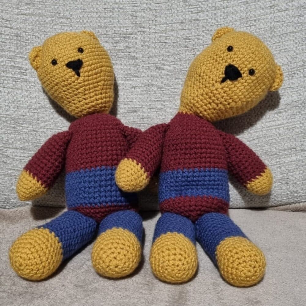 Two crocheted teddy bears with yellow heads, arms, and legs, and maroon and blue bodies sit side by side. - Home Instead