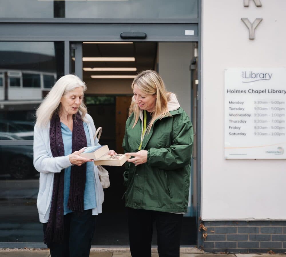 Two women smiling while holding two books and going out of the library