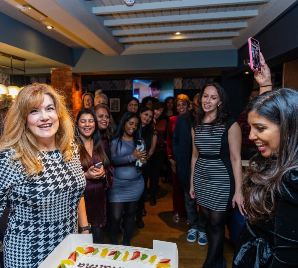 Many women in one room happy and smiling while one of them is blowing a cake
