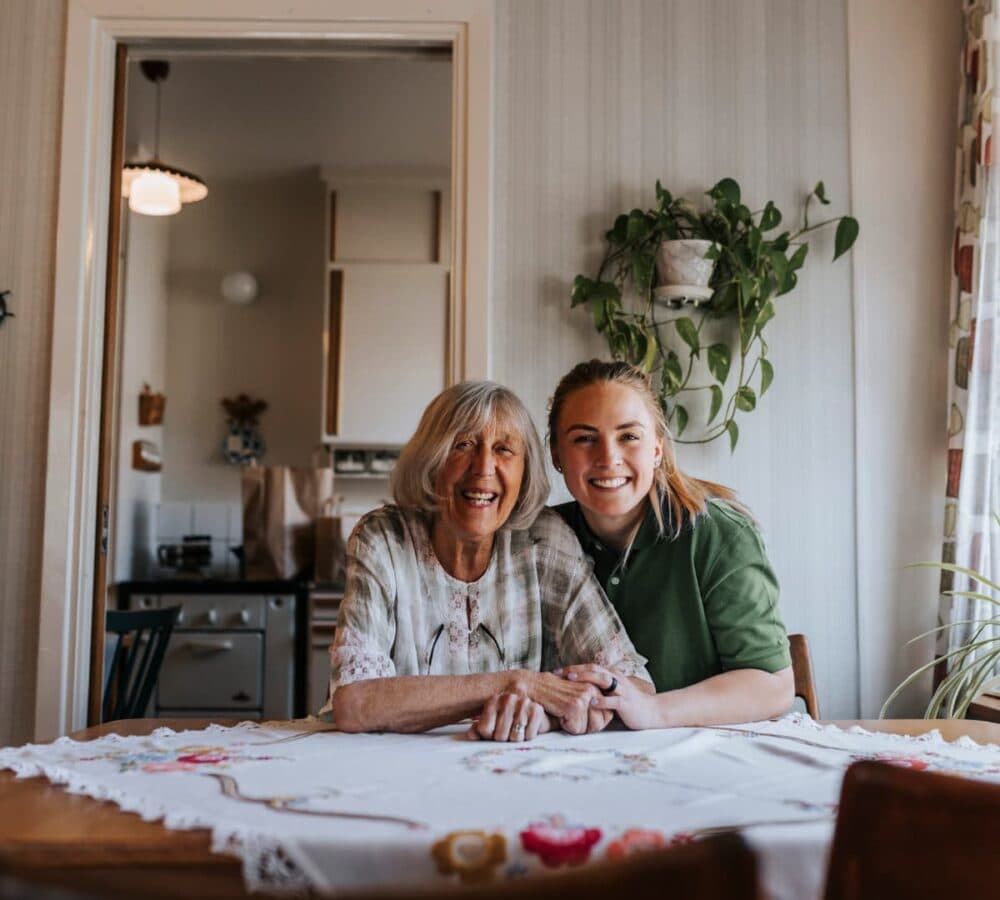 Two women sitting inside the kitchen with a table both happy and smiling