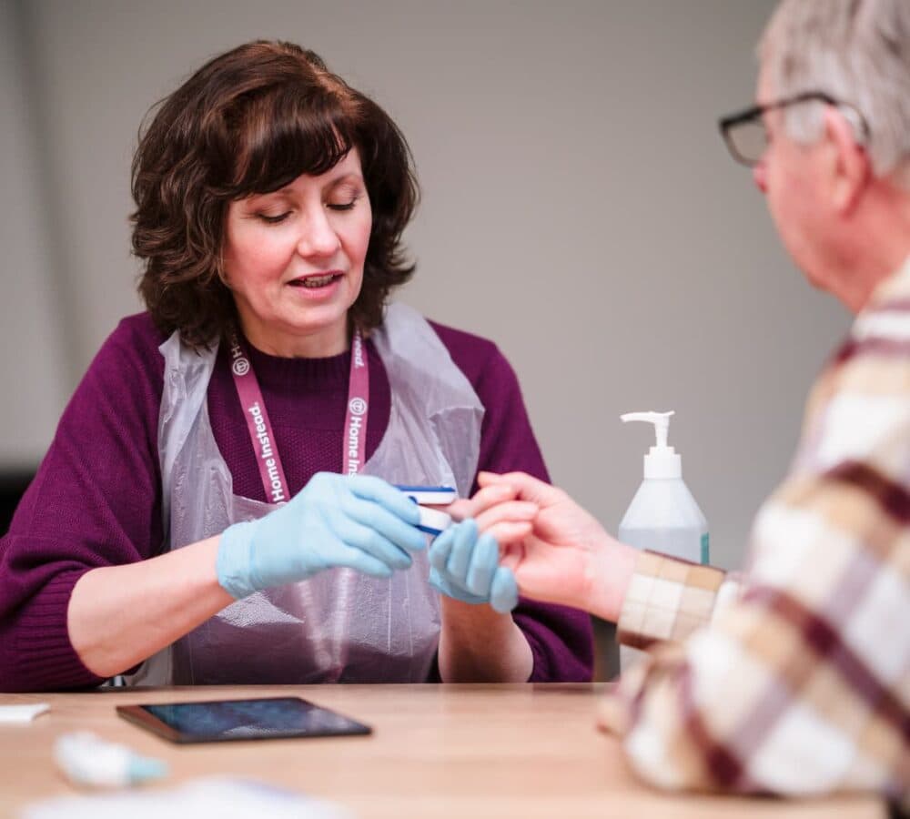 Older man having his nail care with a younger female carer wearing gloves