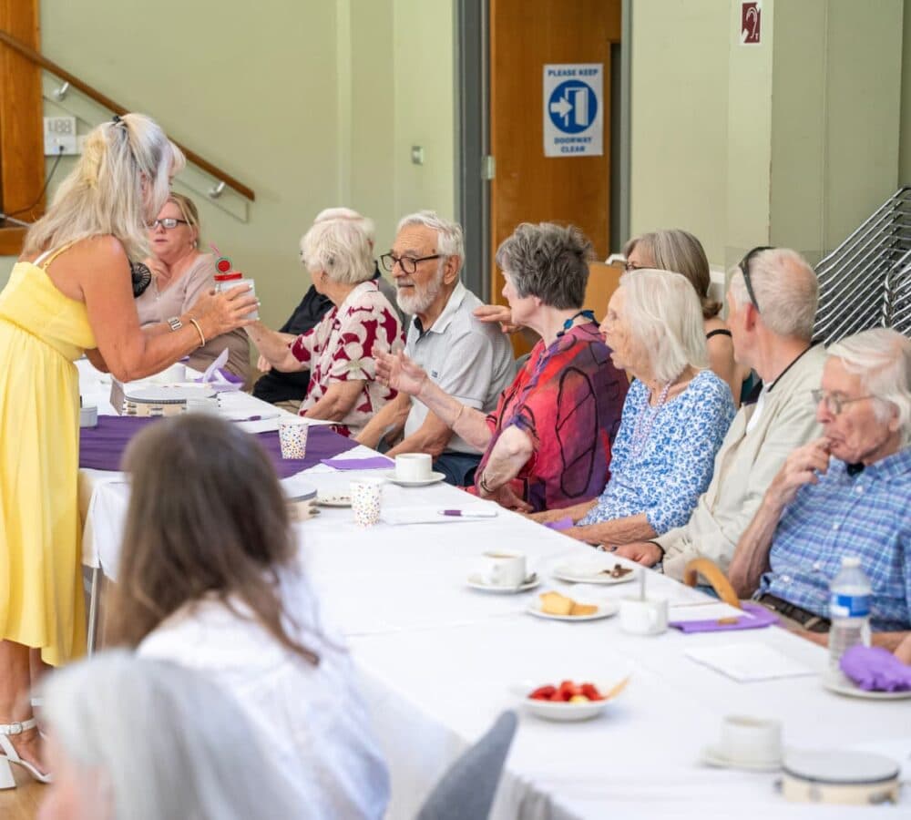 Older adults sitting with a long table happily chatting together inside the hall