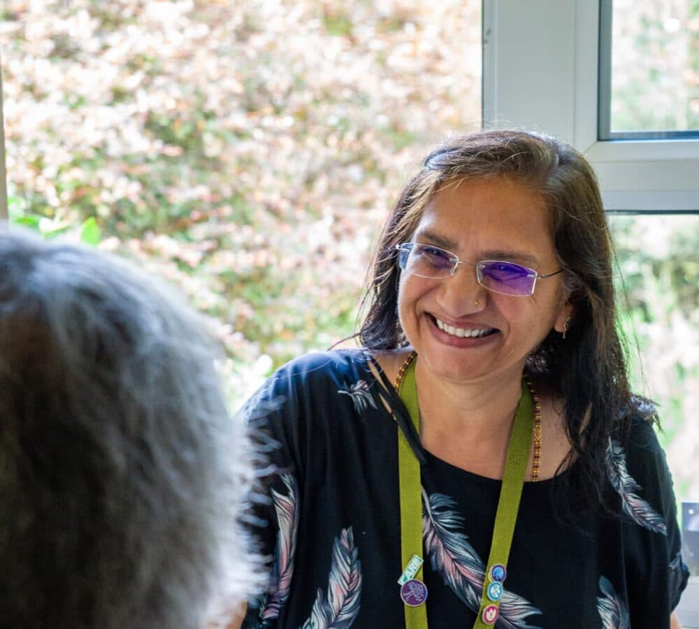 An older male adult with grey hair smiling while welcoming his younger female carer