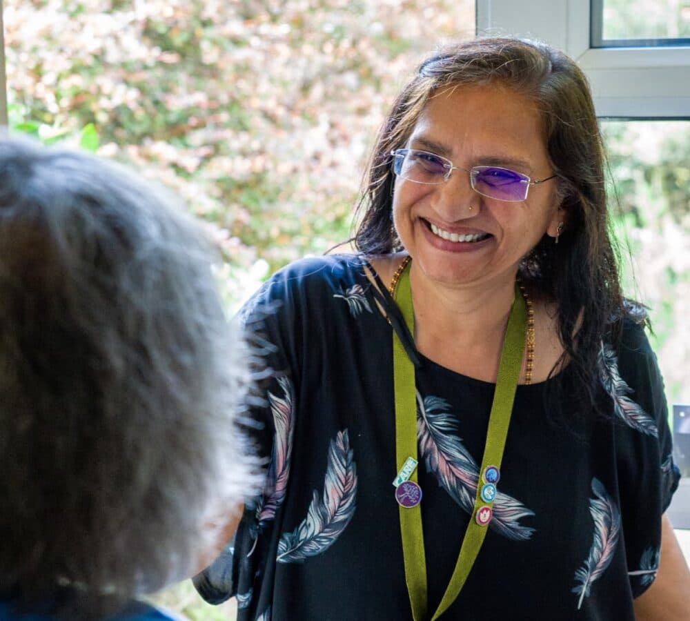 A woman at the door with long black hair and wearing eyeglasses and black shirt with green ID lanyard
