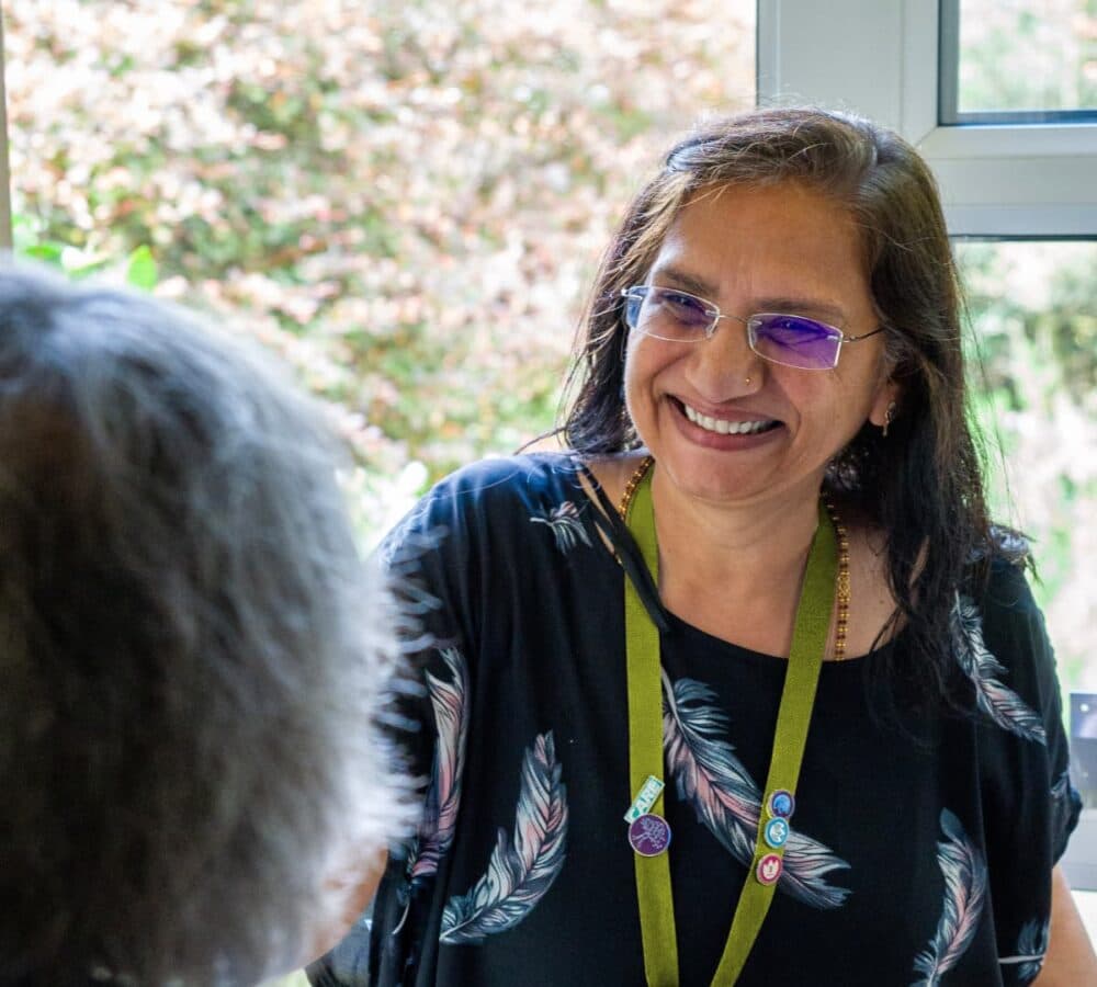 Woman with long black hair and wearing eyeglasses with black top smiling an happy while entering the door
