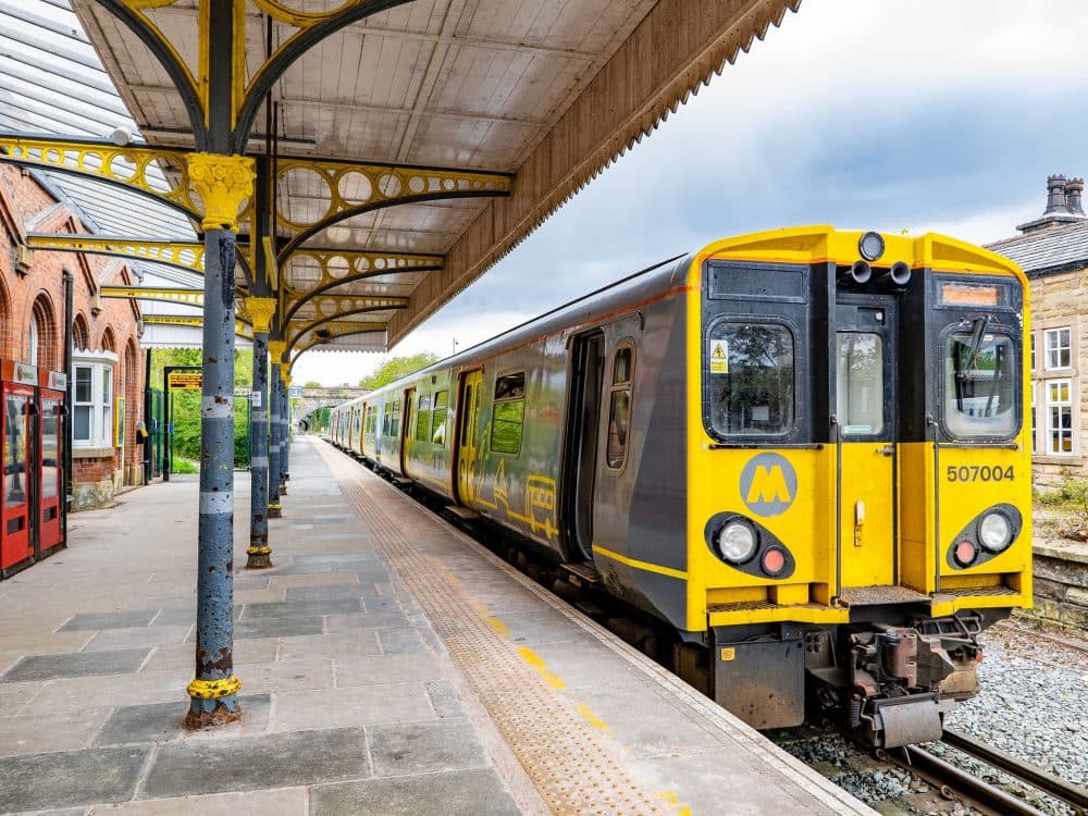 Yellow and grey train stopped at an empty station platform with a covered roof and brick buildings. - Home Instead