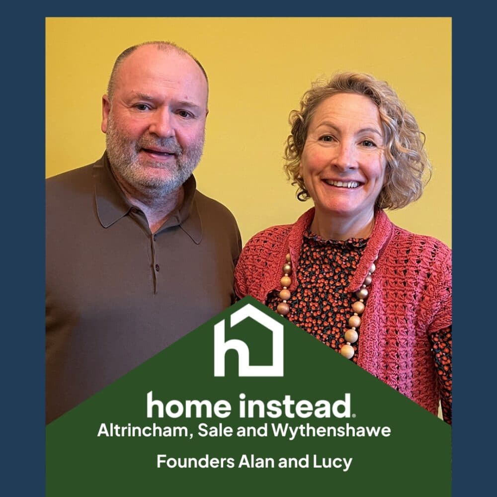 A man and woman smiling, standing together in front of a yellow wall, with text for Home Instead Altrincham. - Home Instead