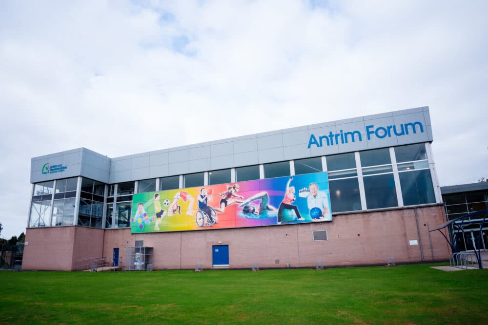 Antrim Forum sports center with large windows and a colorful mural of people doing various sports outside. - Home Instead