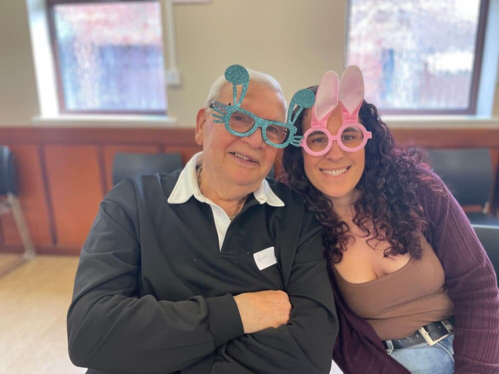 Older man and younger woman smiling, wearing playful bunny ear glasses, sitting closely indoors. - Home Instead