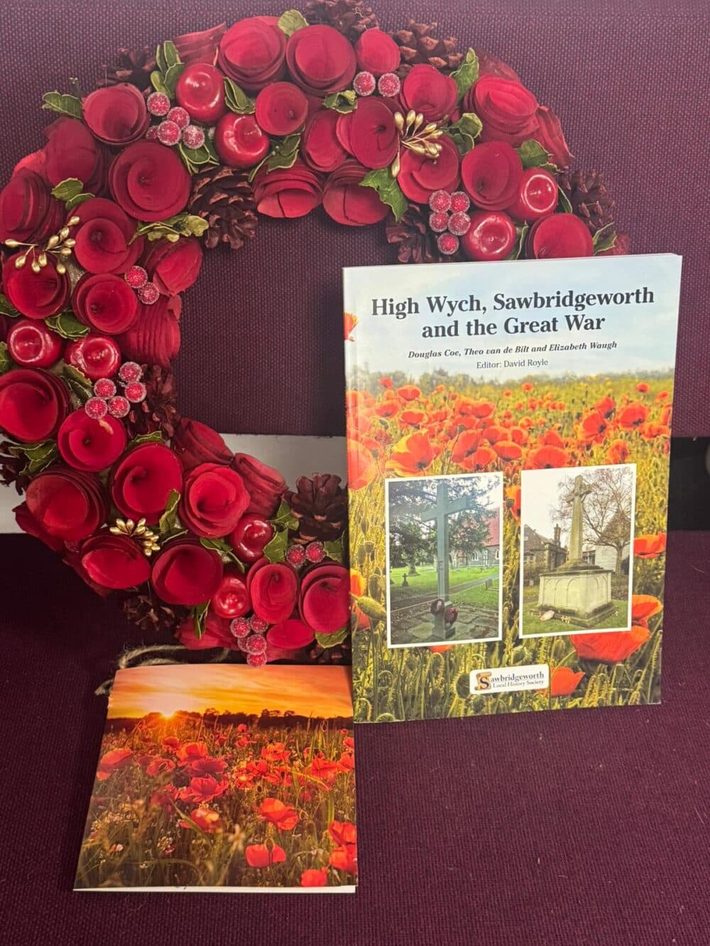 A red floral wreath with two books about poppies and World War I on a purple background. - Home Instead