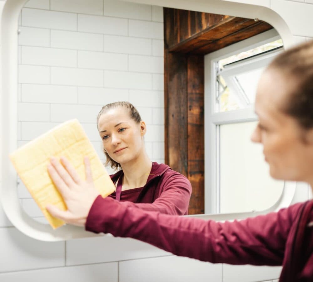 A woman wearing maroon cleaning a mirror by using a wipe