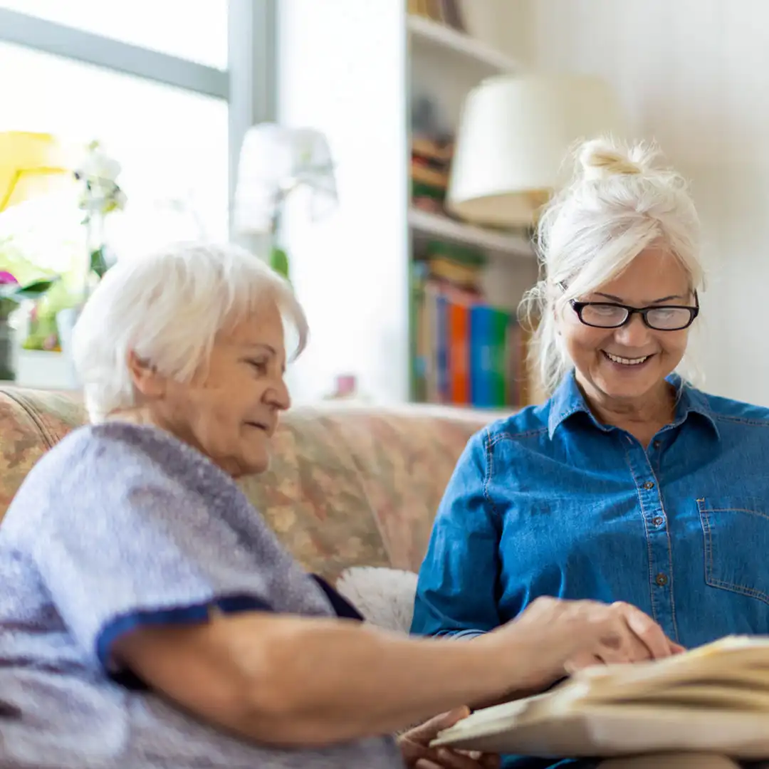 daughter reminiscing looking through a photo album with her senior mum