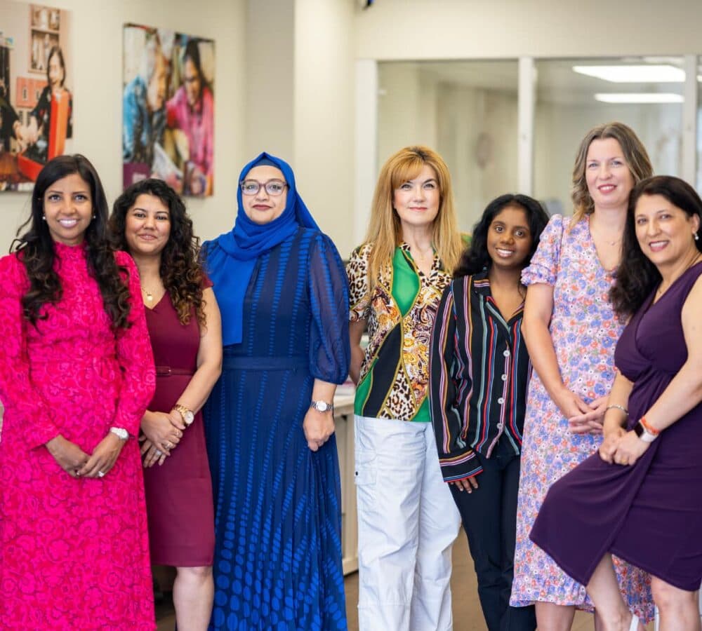 A group of happy women wearing different dress colours standing while inside the office