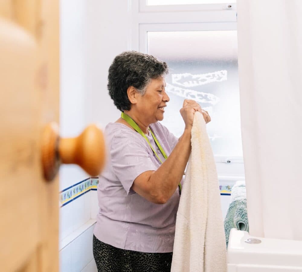 A woman with black hair smiling inside the bathroom while hanging towels