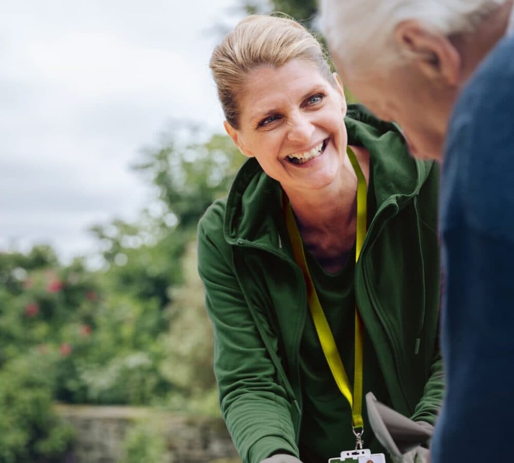 A female carer with blonde hair and wearing green sweater smiling and happy