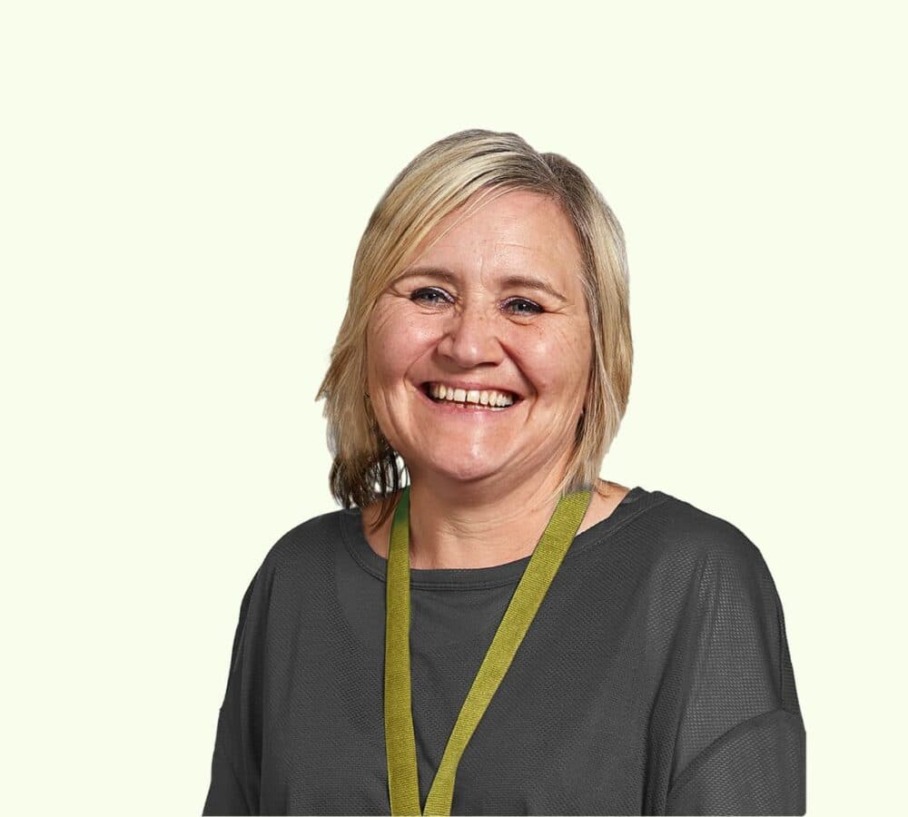 A woman with long curly hair and wearing green sitting on a couch and smiling