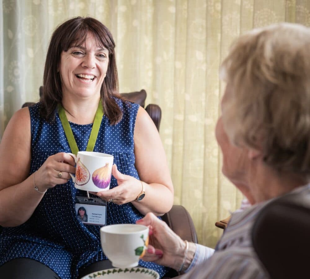 Two women sitting and having a cup of tea together while smiling and chatting together