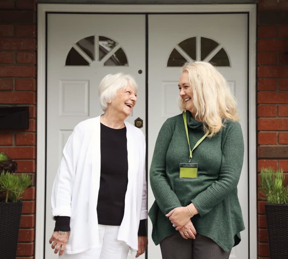 Two women in front of the house door both happy and smiling together