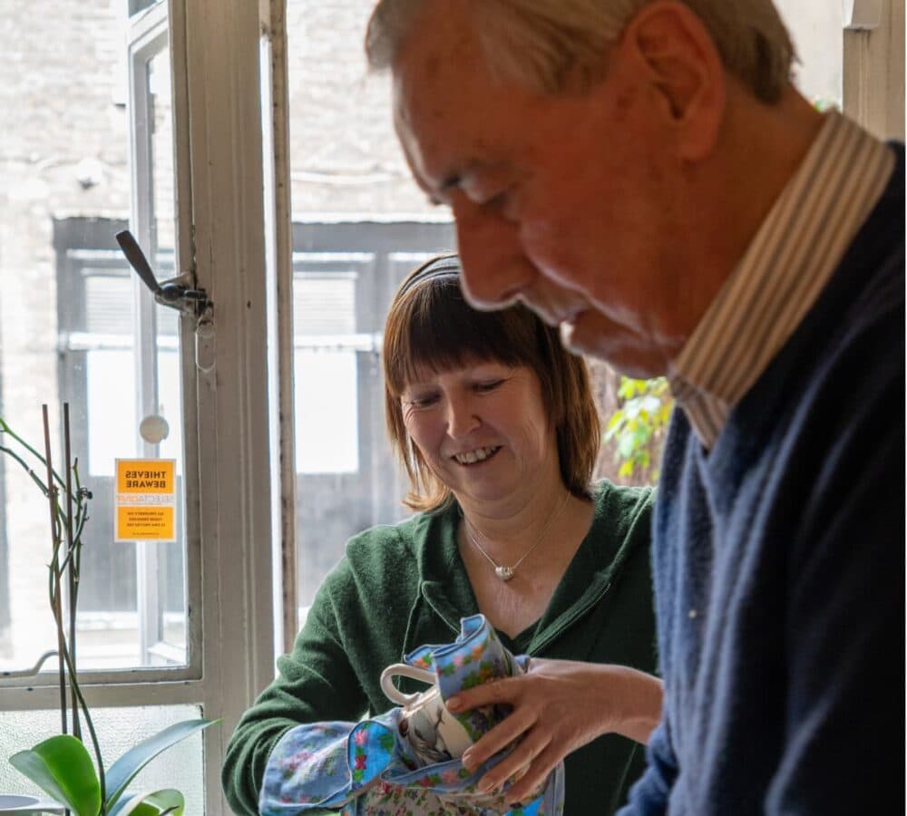 An older male adult with his younger female carer washing the dishes together inside the kitchen